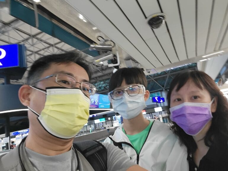 三名戴著口罩與眼鏡的人在機場航廈內自拍