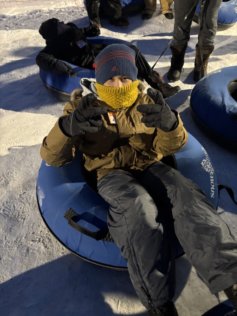 一名戴雪鏡和手套的少年坐在雪圈上